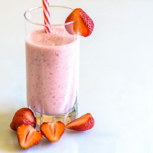 Delicious strawberry smoothie in a glass with fresh strawberries and a striped straw on a light background.