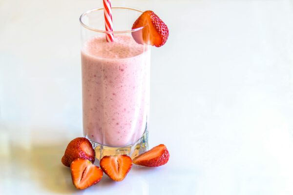 Delicious strawberry smoothie in a glass with fresh strawberries and a striped straw on a light background.