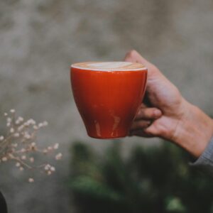 A person holding a vibrant red coffee cup with latte art indoors, offering a cozy vibe.