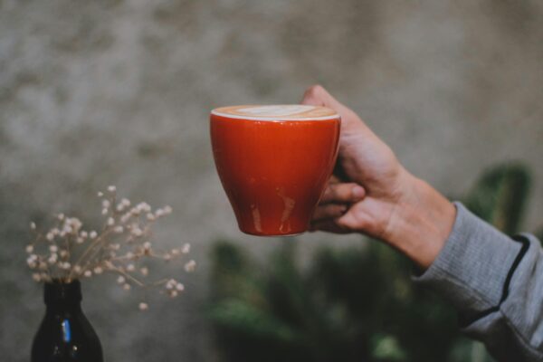 A person holding a vibrant red coffee cup with latte art indoors, offering a cozy vibe.