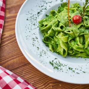 Delicious fettuccine pasta tossed in vibrant green pesto, garnished with a cherry tomato, perfect for an Italian-style meal.