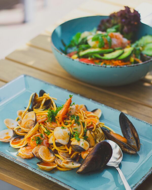 Seafood pasta served outdoors, featuring shrimp, mussels, and fresh vegetables, perfect for food enthusiasts.