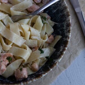 Close-up of creamy fettuccine pasta with salmon and herbs in a rustic bowl.