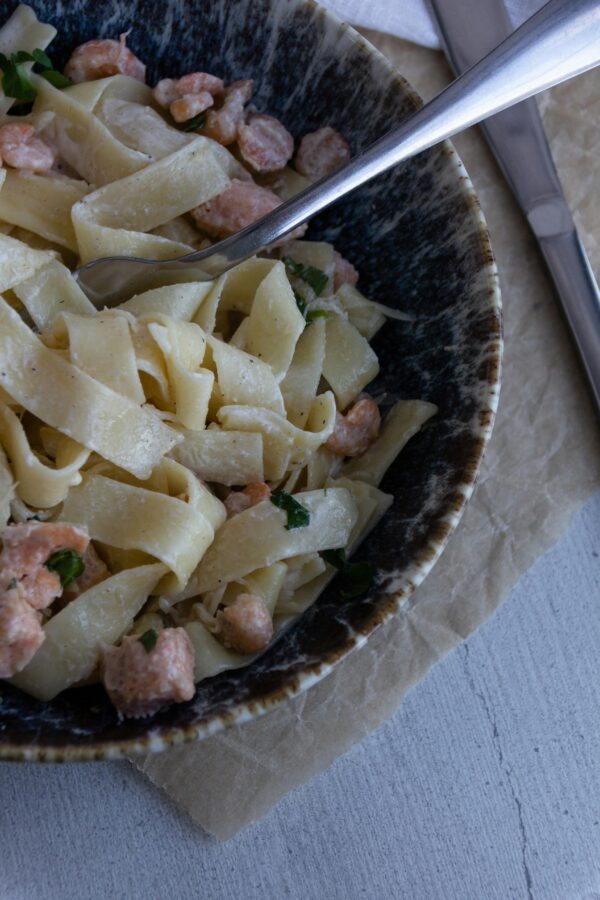 Close-up of creamy fettuccine pasta with salmon and herbs in a rustic bowl.