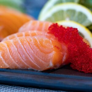 Close-up of fresh salmon sashimi topped with bright red caviar and garnished with lemon slices.