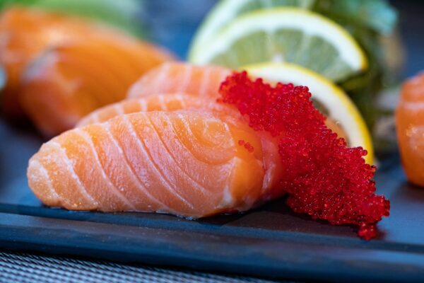 Close-up of fresh salmon sashimi topped with bright red caviar and garnished with lemon slices.