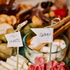 Close-up of a charcuterie board featuring salami, dill havarti cheese, and garnishes.