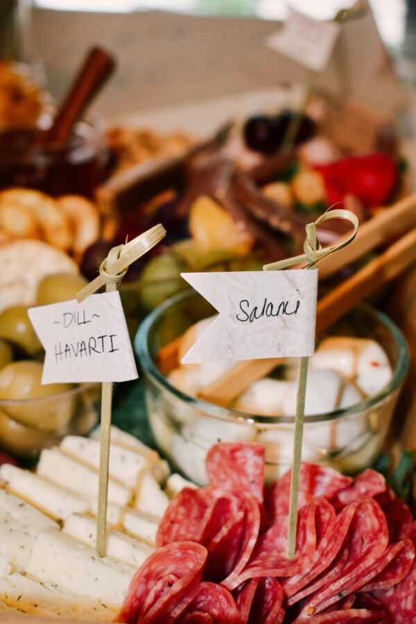 Close-up of a charcuterie board featuring salami, dill havarti cheese, and garnishes.