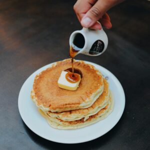 Delicious stack of pancakes topped with butter and maple syrup being poured.