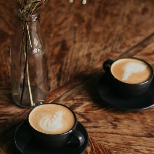 Aesthetic café setting with two cappuccinos on a wooden table and dried flowers.