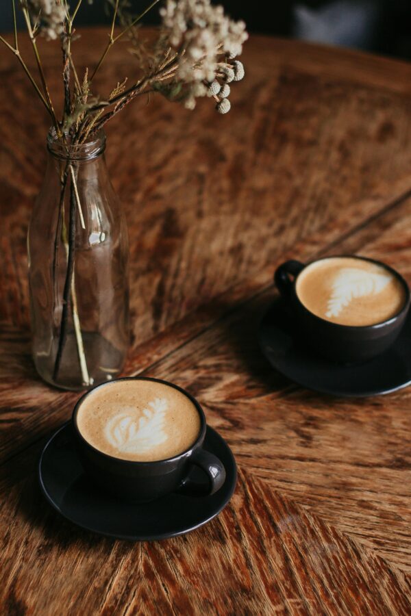 Aesthetic café setting with two cappuccinos on a wooden table and dried flowers.