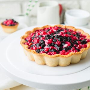 Homemade berry tart with fresh blackberries and currants on a white plate.