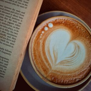 A cappuccino with heart latte art beside an open book, perfect for a cozy reading session indoors.