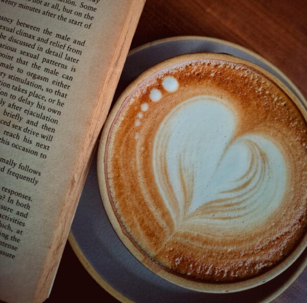 A cappuccino with heart latte art beside an open book, perfect for a cozy reading session indoors.