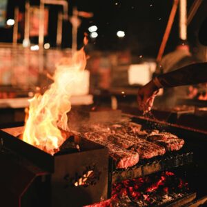 Vibrant night scene of a BBQ grill with sizzling meat and dancing flames.