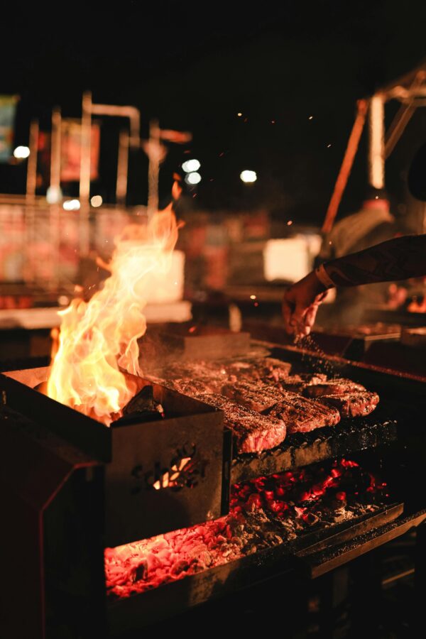 Vibrant night scene of a BBQ grill with sizzling meat and dancing flames.