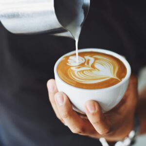 Close-up of a barista pouring milk to create latte art in a coffee cup.