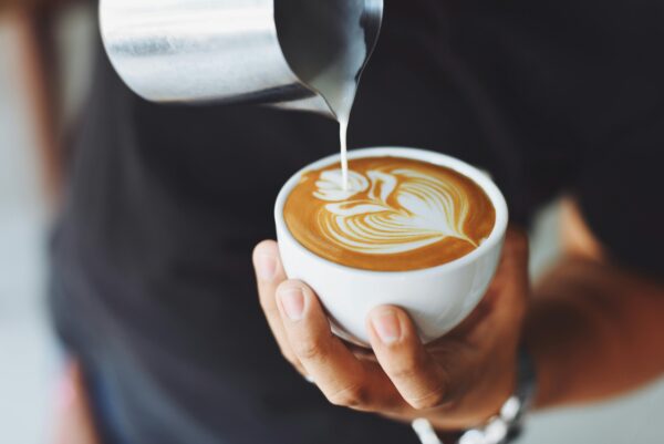 Close-up of a barista pouring milk to create latte art in a coffee cup.