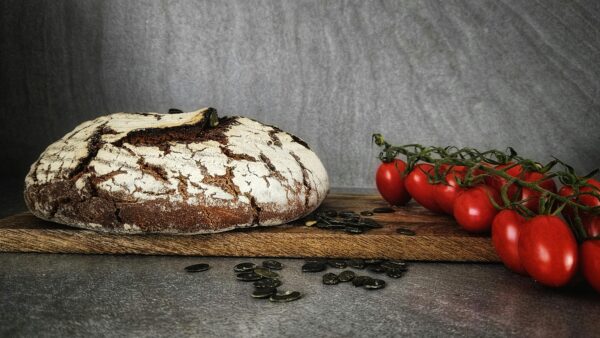 Crisp rustic bread and vine tomatoes on a wooden board with pumpkin seeds.