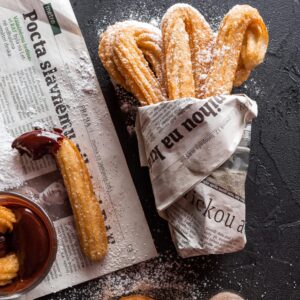 Freshly made churros dusted with sugar, wrapped in newspaper, with chocolate sauce.