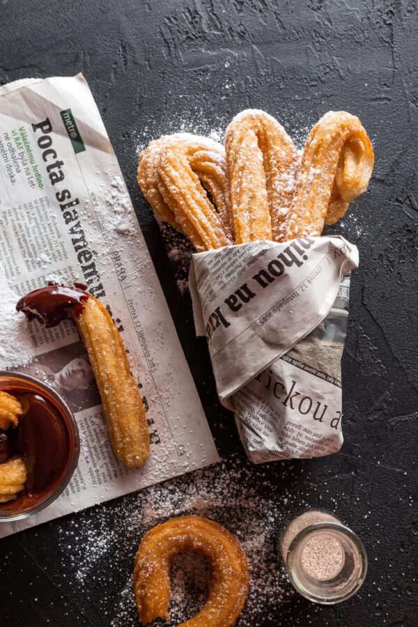 Freshly made churros dusted with sugar, wrapped in newspaper, with chocolate sauce.