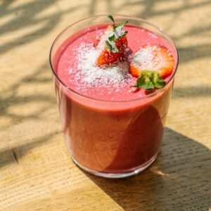 Refreshing strawberry smoothie topped with coconut flakes in natural light on a wooden table.