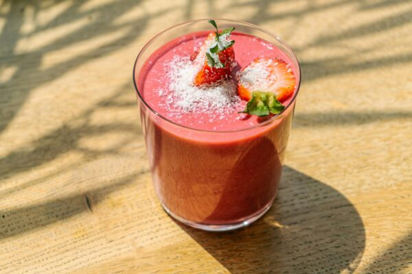 Refreshing strawberry smoothie topped with coconut flakes in natural light on a wooden table.