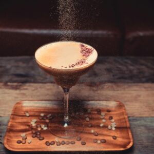 A stylish coffee cocktail dusted with garnish on a wooden tray, perfect for cozy settings.