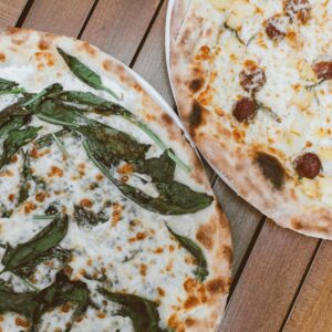 Close-up of two flavorful pizzas with fresh toppings on a wooden table.