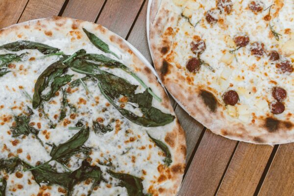 Close-up of two flavorful pizzas with fresh toppings on a wooden table.