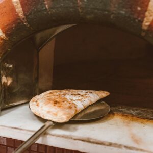 A calzone being taken out of a traditional Italian brick oven, showcasing rustic baking style.