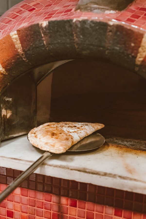 A calzone being taken out of a traditional Italian brick oven, showcasing rustic baking style.