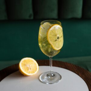 A citrusy lemon cocktail with ice in a wine glass on a wooden table, perfect for a refreshing drink.