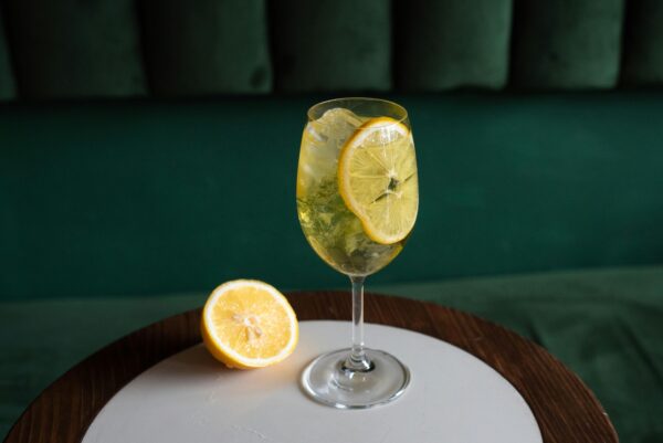 A citrusy lemon cocktail with ice in a wine glass on a wooden table, perfect for a refreshing drink.