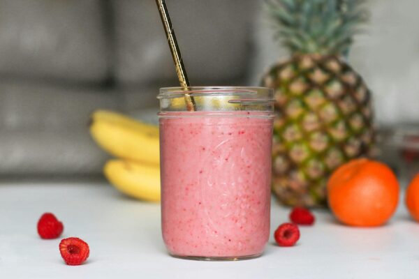 A refreshing pink smoothie made with bananas, raspberries, and tropical fruits in a glass jar.