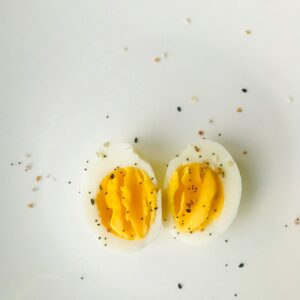 A close-up of a sliced boiled egg with pepper seasoning on a white plate, ideal for healthy meals.