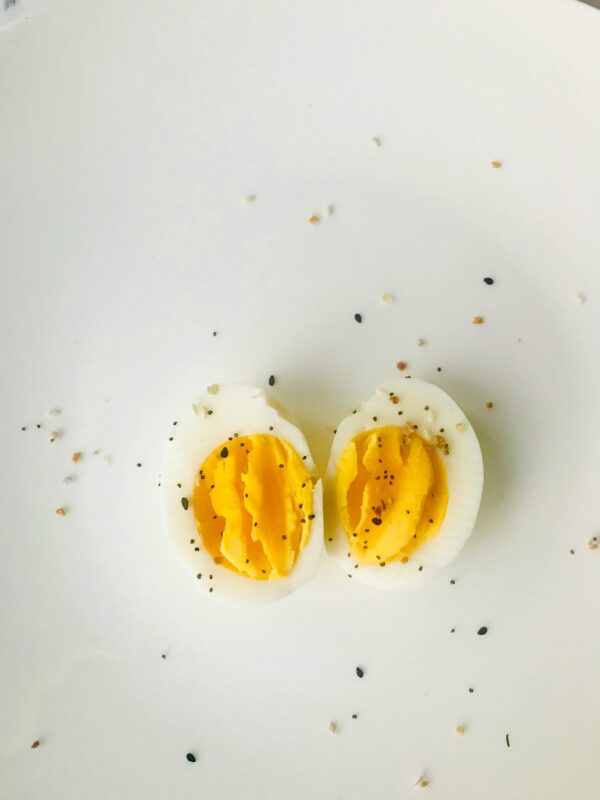 A close-up of a sliced boiled egg with pepper seasoning on a white plate, ideal for healthy meals.