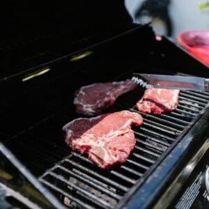 Close-up of juicy steaks on an outdoor grill, held with tongs, perfect for barbecue enthusiasts.