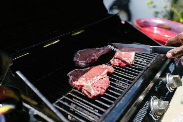 Close-up of juicy steaks on an outdoor grill, held with tongs, perfect for barbecue enthusiasts.