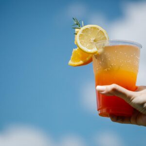 Vibrant tequila sunrise cocktail with lemon and orange slices held against a clear blue sky.