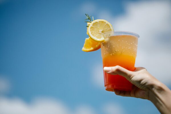 Vibrant tequila sunrise cocktail with lemon and orange slices held against a clear blue sky.