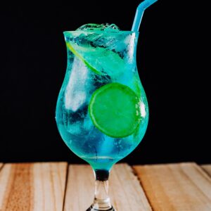 A refreshing blue lagoon cocktail served with ice and a slice of lime on a wooden table.