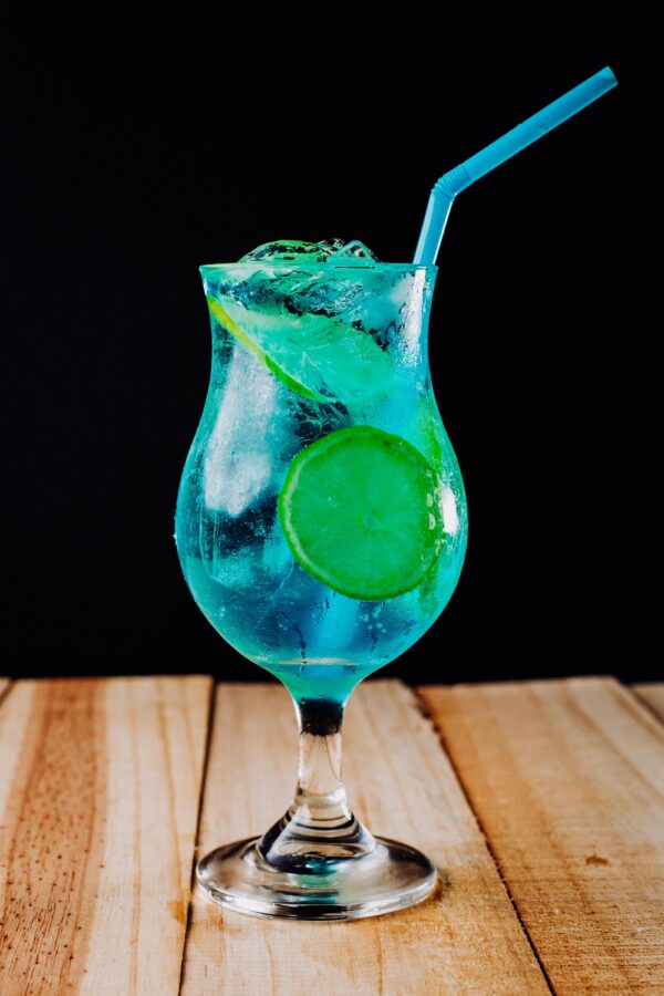 A refreshing blue lagoon cocktail served with ice and a slice of lime on a wooden table.