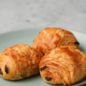 Three flaky chocolate croissants displayed on a pastel plate, perfect for breakfast.