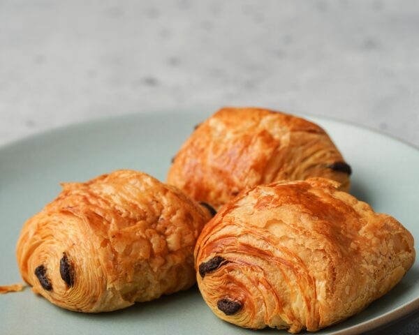 Three flaky chocolate croissants displayed on a pastel plate, perfect for breakfast.