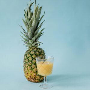 Pineapple and glass of juice on a blue surface, emphasizing tropical freshness.