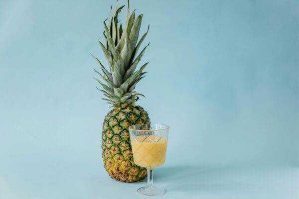 Pineapple and glass of juice on a blue surface, emphasizing tropical freshness.